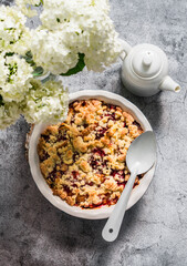 Raspberry peaches crumble in a baking dish on a gray background, top view. Summer dessert
