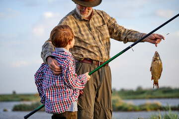 Fisherman with grandson enjoys in fishing on river. Sport, recreation, lifestyle. Happy child boy...