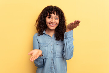 Young mixed race woman isolated on yellow background makes scale with arms, feels happy and confident.