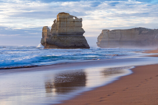 Reflection of a rugged sea stack and cliffs on a wet sandy beach at twilight