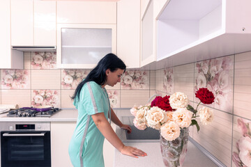 Tired woman in the kitchen. A woman is standing near the sink in the kitchen