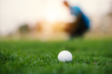 Green grass with golf ball close-up in soft focus at sunlight and have blur background with man playing golf end game successful.