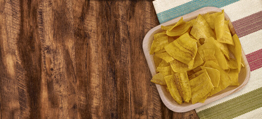 Crispy Banana Chips. Fried or baked sliced banana. Top view of typical traditional dish of Latin American gastronomy called Chifles or fried tostones on a wooden table. Roasted banana. Snack.