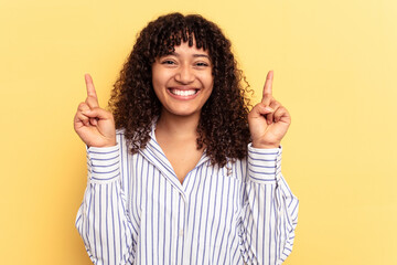 Young mixed race woman isolated on yellow background indicates with both fore fingers up showing a...