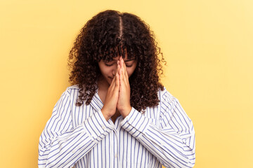 Fototapeta na wymiar Young mixed race woman isolated on yellow background praying, showing devotion, religious person looking for divine inspiration.