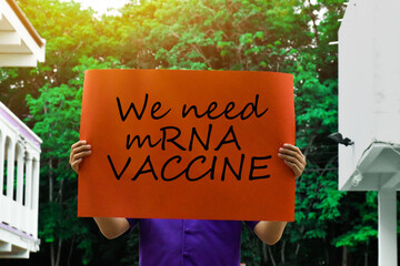 Orange label with text “We need mRNA VACCINE ” holding in hands with trees and the sun light in background