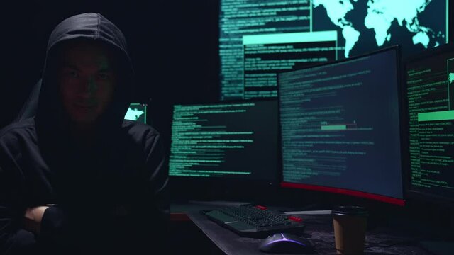 Asian Male Hacker Pose With Code On Multiple Computer Screens And Downloading Data
