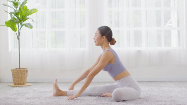 Happy Athletic Asian woman practice yoga stretching pose for stretching muscle for warm up with meditation smile,Healthy female doing yoga exercise and relax at home,Yoga Healthcare Concept