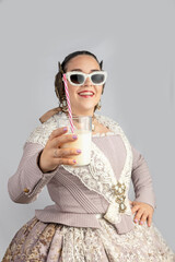 Young fallera with sunglasses shows a glass of horchata