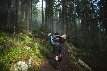 A mountain bike rider carries a bike on his back on a trail in the woods. Mountain biker overcomes the way up with a bicycle on his back