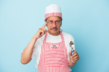 Senior indian ice cream man holding a scoop isolated on blue background pointing temple with finger, thinking, focused on a task.