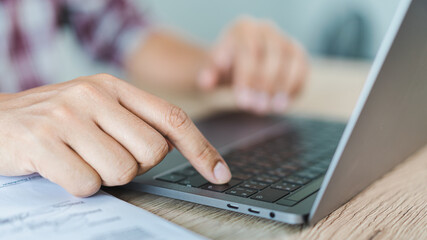 Cropped close-up image of a businessman`s hands typing working on a laptop at the home office. Freelancer, remote occupation, tutor, student e-learning concept