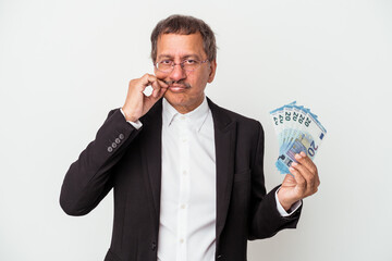 Middle aged indian business man holding bills isolated on white background with fingers on lips keeping a secret.