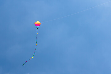 Child's rainbow coloured diamond kite with tail flying high in clear blue summer sky