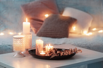 Christmas decoration   with burning candles on  white table against the background of  sofa with...