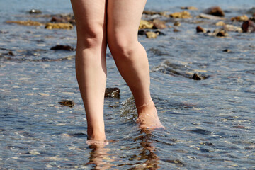 Barefoot woman walking by the water in the sea waves. Naked female legs in water, beach vacation