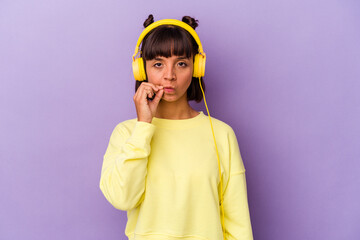 Young mixed race woman listening to music isolated on purple background with fingers on lips keeping a secret.