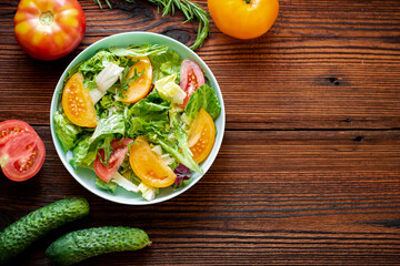 Healthy salad of fresh vegetables, herbs and tomatoes on a wooden background. Place for your text.