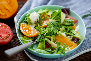 Healthy salad of fresh vegetables, herbs and tomatoes on a wooden background.