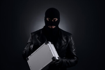 Man wearing knitted balaclava with metal briefcase on black background