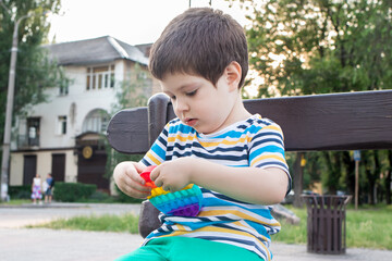 A child of 4 years plays with Pop It in the city park. Anti-stress toy for the development of fine...