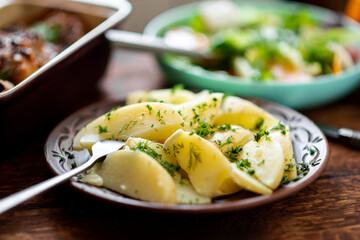Boiled young potatoes with dill, fresh vegetable salad and baked chicken thighs on a dark wooden...