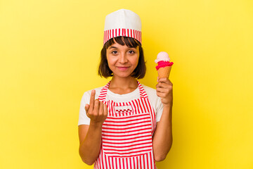 Young mixed race ice cream maker woman holding an ice cream isolated on yellow background pointing with finger at you as if inviting come closer.