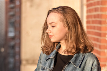 Portrait of a young teenage girl against a brick wall at sunset