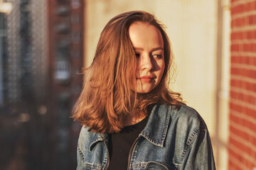 Portrait of a young teenage girl against a brick wall at sunset