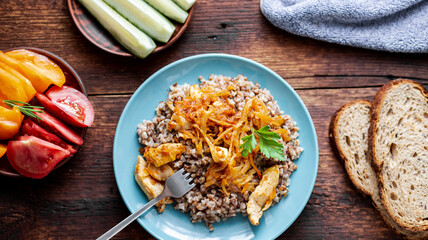 Buckwheat porridge with meat, onions and carrots on a wooden background. With fresh vegetables, cucumbers and tomatoes.