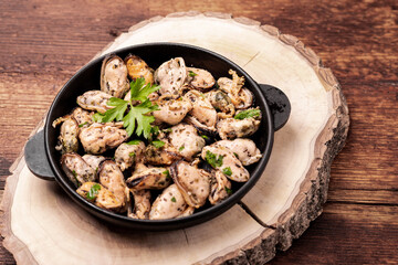 Peeled mussels in sauce on a dark wooden background.