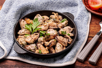 Peeled mussels in sauce on a dark wooden background.