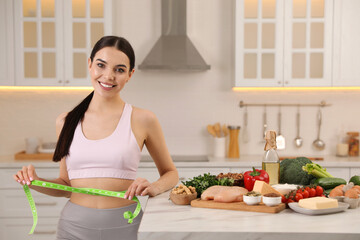 Happy woman measuring waist with tape in kitchen. Keto diet