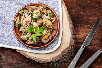 Peeled mussels in sauce on a dark wooden background.