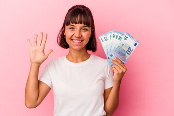 Young mixed race woman holding bills isolated on pink background smiling cheerful showing number five with fingers.