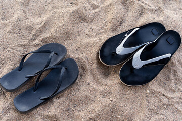Men's and women's beach shoes on the sand under the rays of the sun. Two pairs of black flip-flops