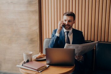 Business owner talking on phone after reading news, sitting in cafe