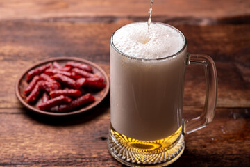 Glass of beer and snacks- dried sausages on a wooden background. Beer is poured into the glass.