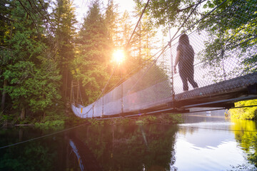 Woman Walking on Suspension Bridge over the water in Green and Vibrant Rain Forest during a sunny...