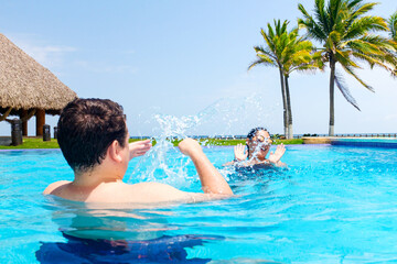 Happy biracial couple having fun and splashing water in the pool by the beach