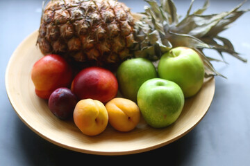 Wooden bowl with various colorful fruit on dark background. Selective focus.