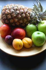 Wooden bowl with various colorful fruit on dark background. Selective focus.