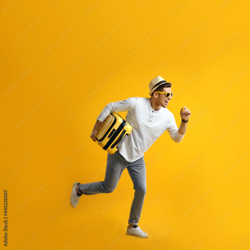 Poster Male tourist with suitcase running on yellow background