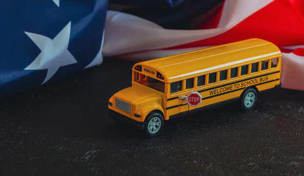 School bus and American flag. 
School bus and American flag lie on a black background, close-up side view.