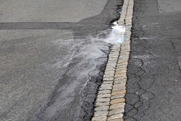 Road with a pothole. There is a puddle of rain water in the pothole. The water is splashed around...