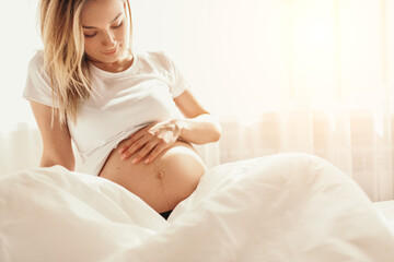 Obraz na płótnie Canvas Pregnant woman stroking belly in bed