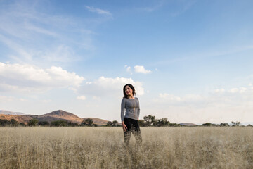 Naklejka na ściany i meble Young adult Mexican woman standing in a dry grassy meadow looking away