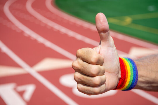 Gay athlete with rainbow pride  wristband gives thumbs up gesture in front of a sports track background
