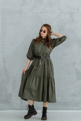 Naklejka premium a woman in a green long dress, sunglasses and rough black shoes on a gray background. trending women's fashion clothing 2021.