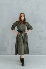 Naklejka premium a woman in a green long dress, sunglasses and rough black shoes on a gray background. trending women's fashion clothing 2021.